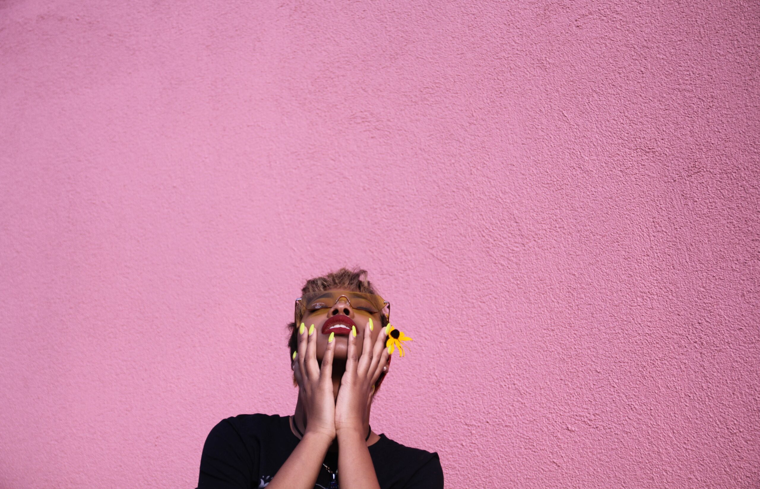 trendy-young-black-woman-touching-face-while-throwing-head-back-on-pink-background