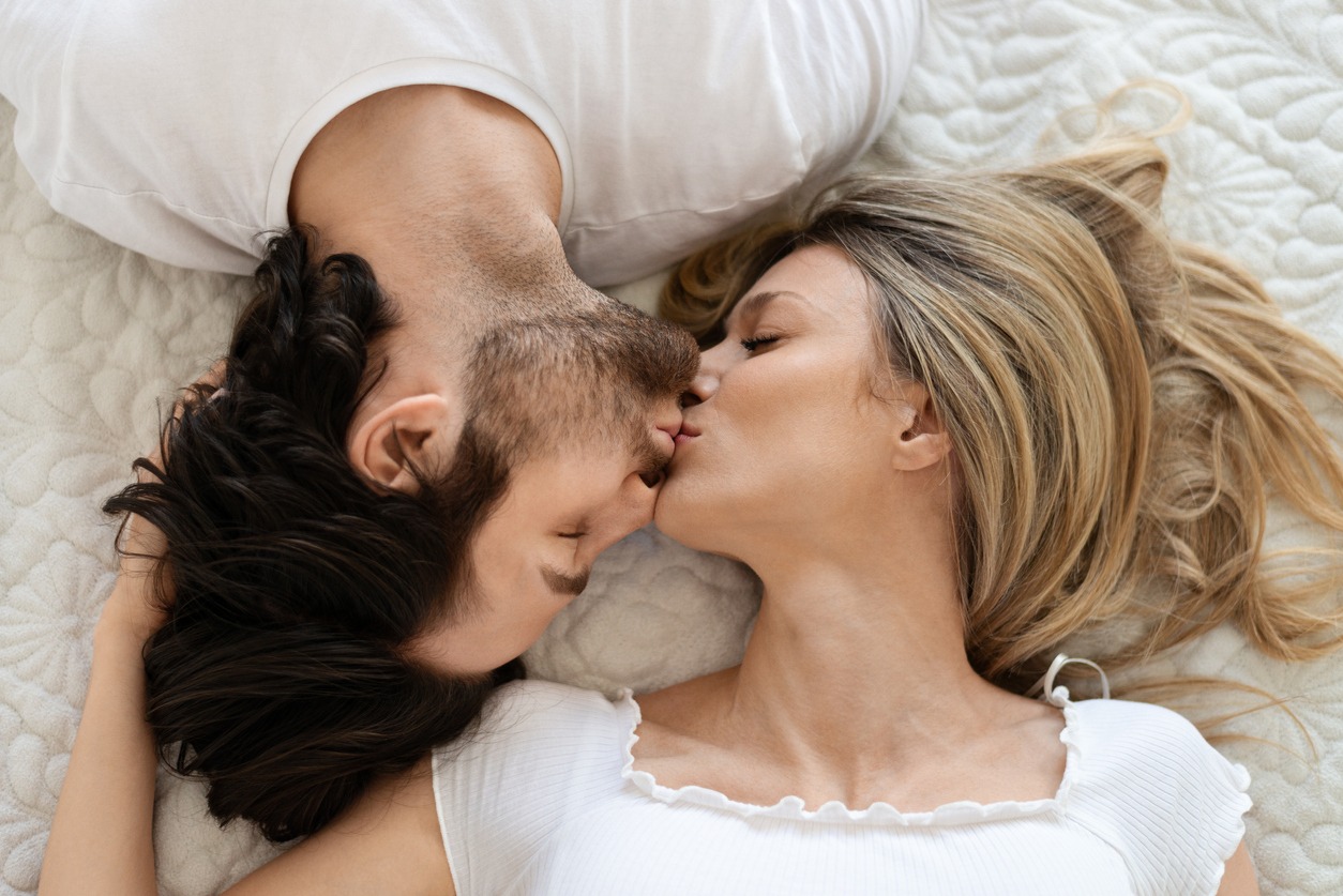 Top view of loving caucasian couple kissing and cuddling, lying in bed, expressing affection and love